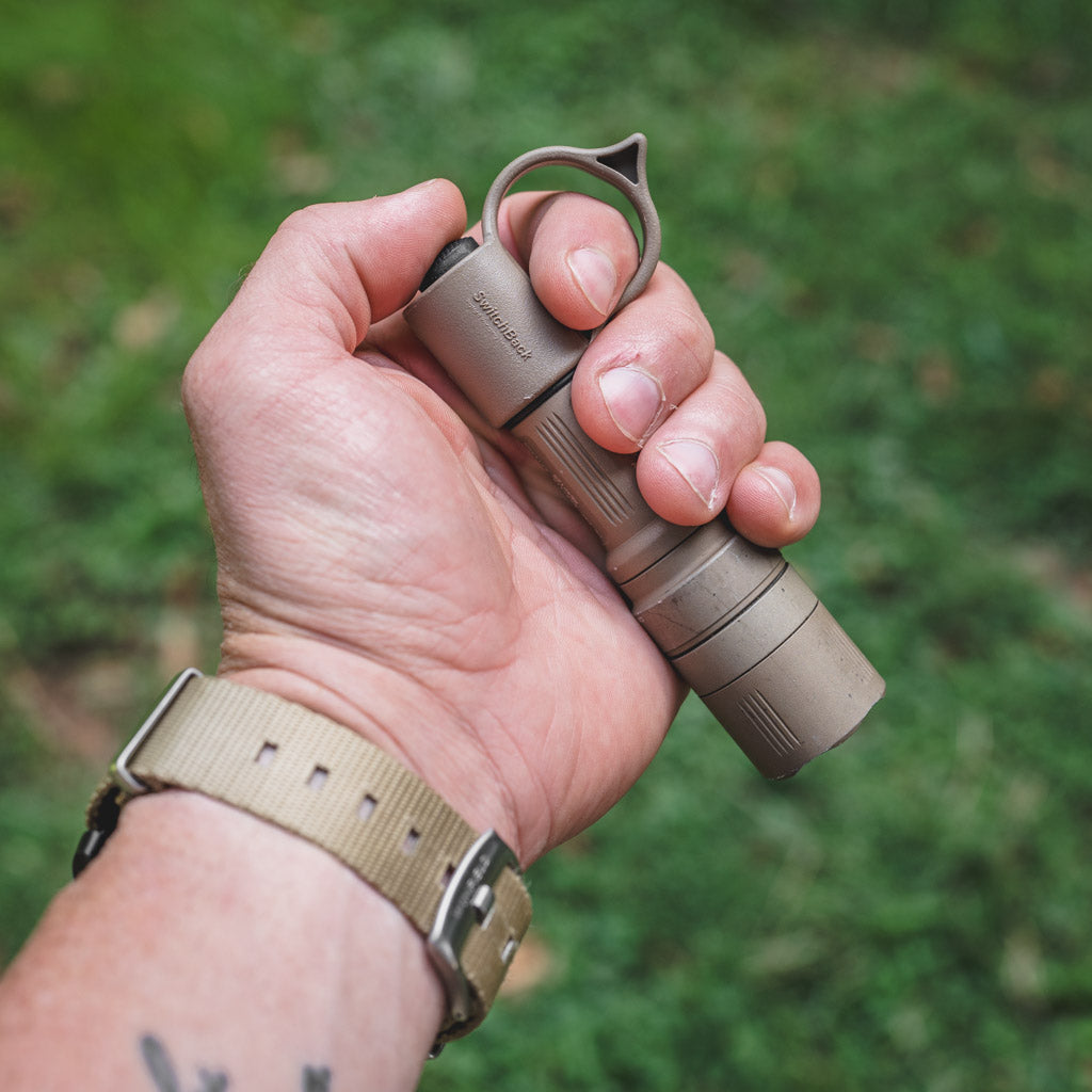Hand holding a SureFire flashlight with the finger ring of a Thyrm SwitchBack S