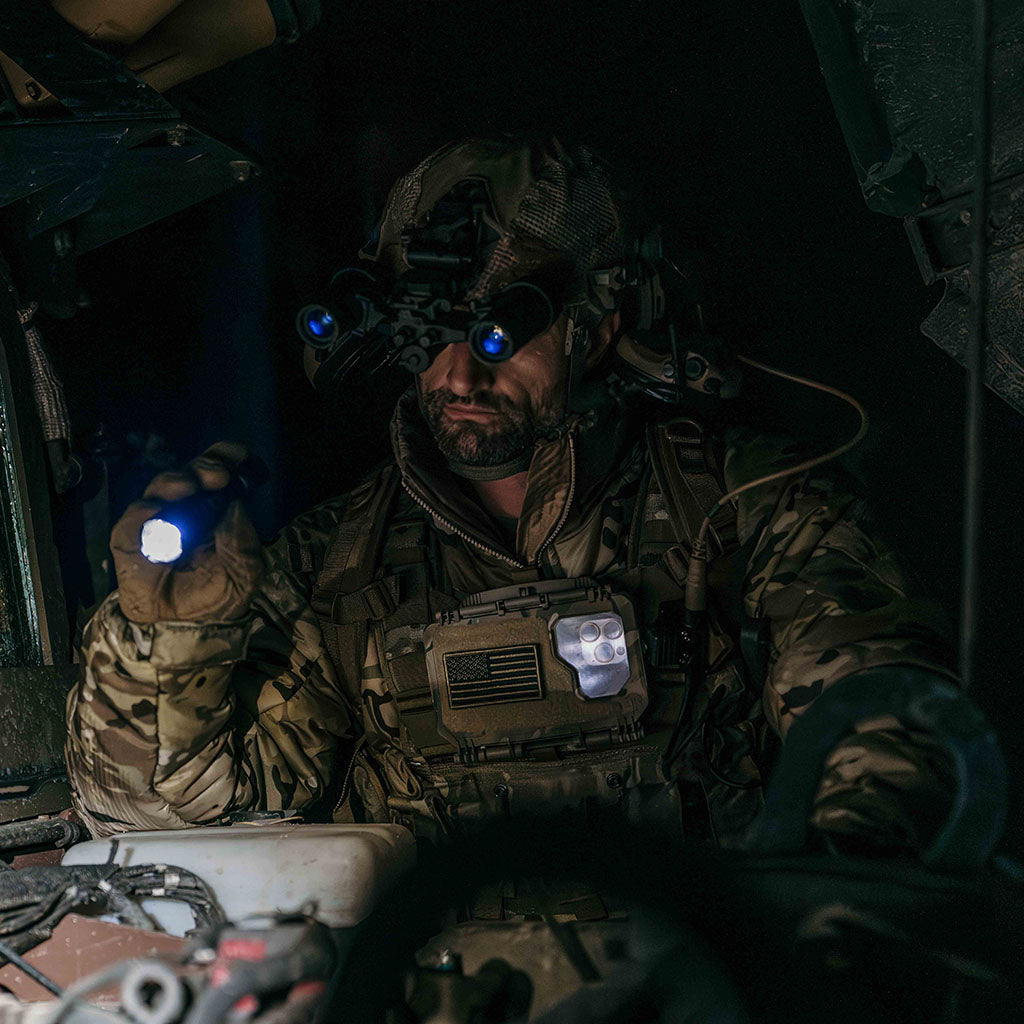 Soldier in camouflage gear with night vision goggles, a flashlight, and a Thyrm DarkVault Comms 2.0 Case attached to his plate carrier