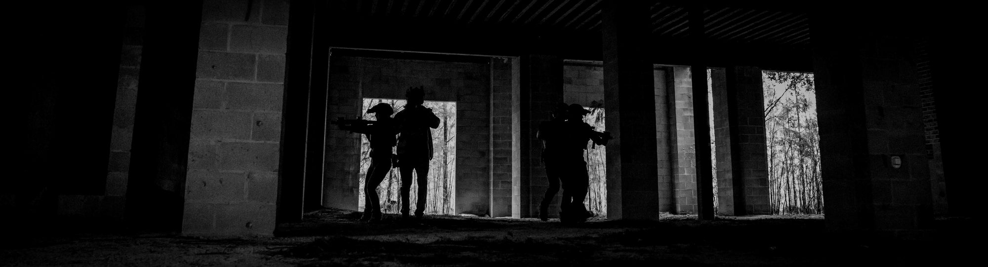 Silhouetted tactical team with searching an unfinished building at dusk, black and white, rugged wilderness gear.