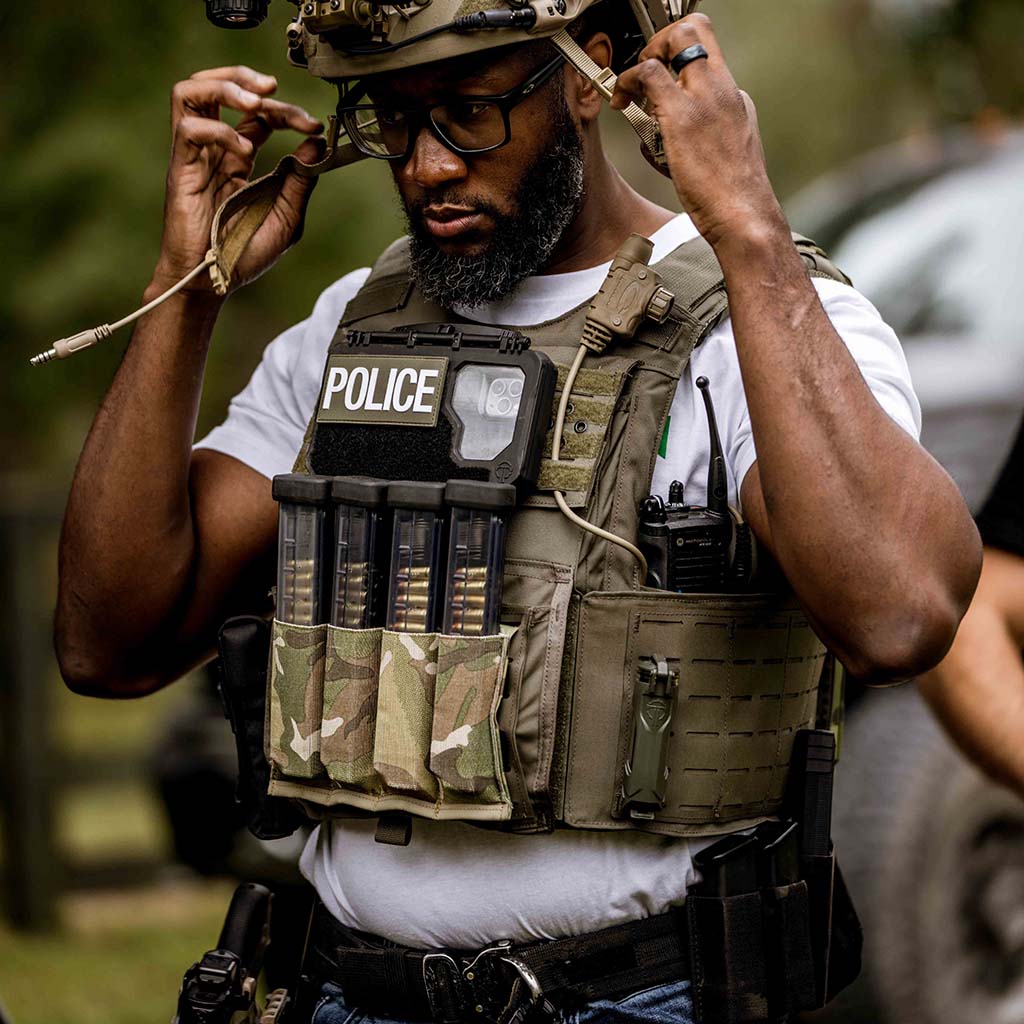 Police person putting on a helmet. He wears a DarkVault Comms 2.0 Case on his duty vest.
