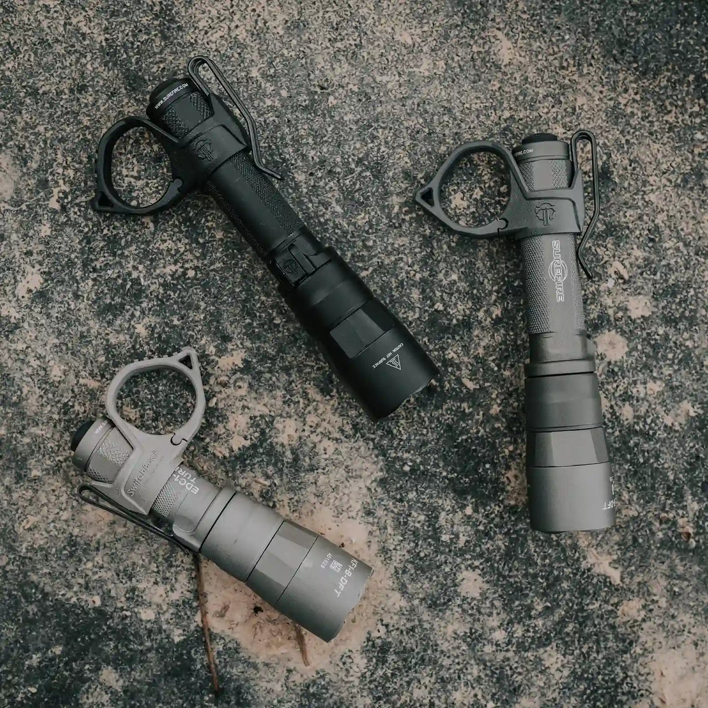 Three Surefire flashlights with Thyrm SwitchBacks on a textured surface