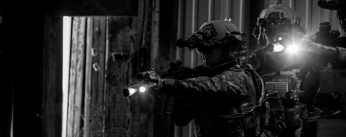 Two individuals in tactical gear with flashlights at night.