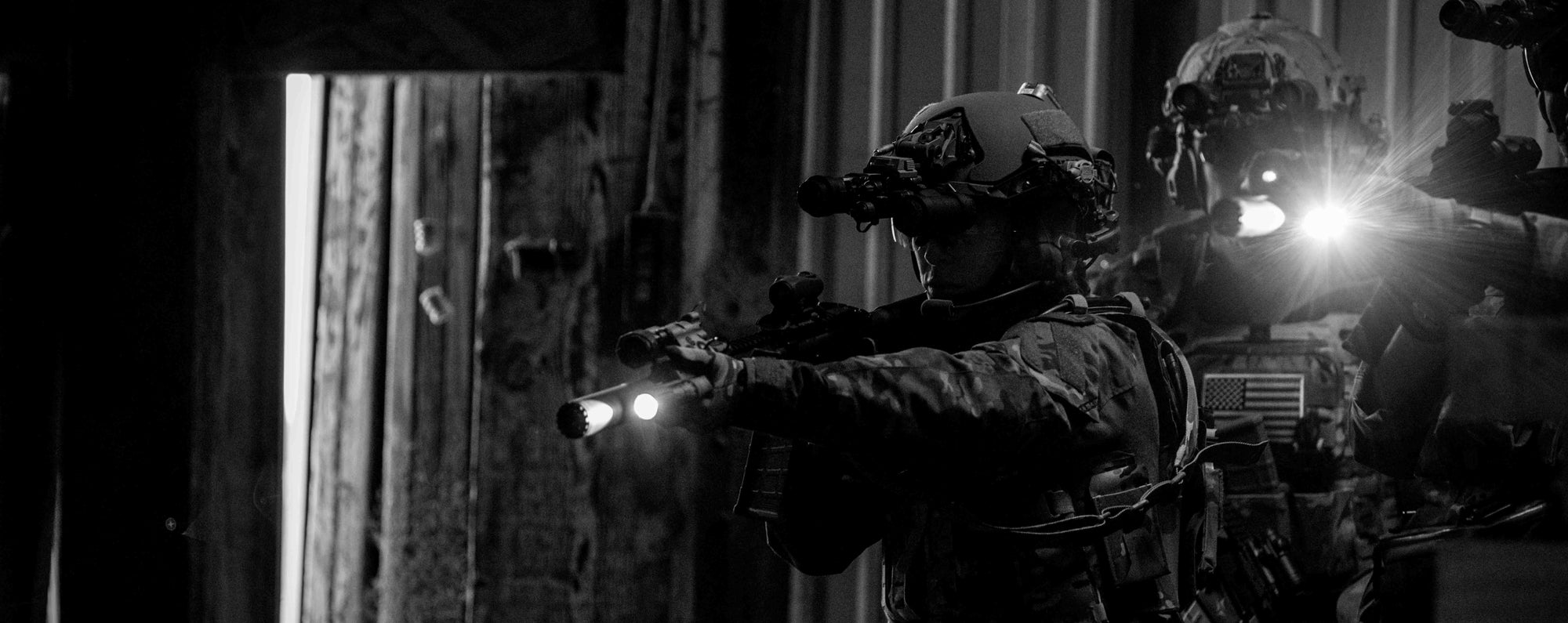 Two individuals in tactical gear with flashlights at night.