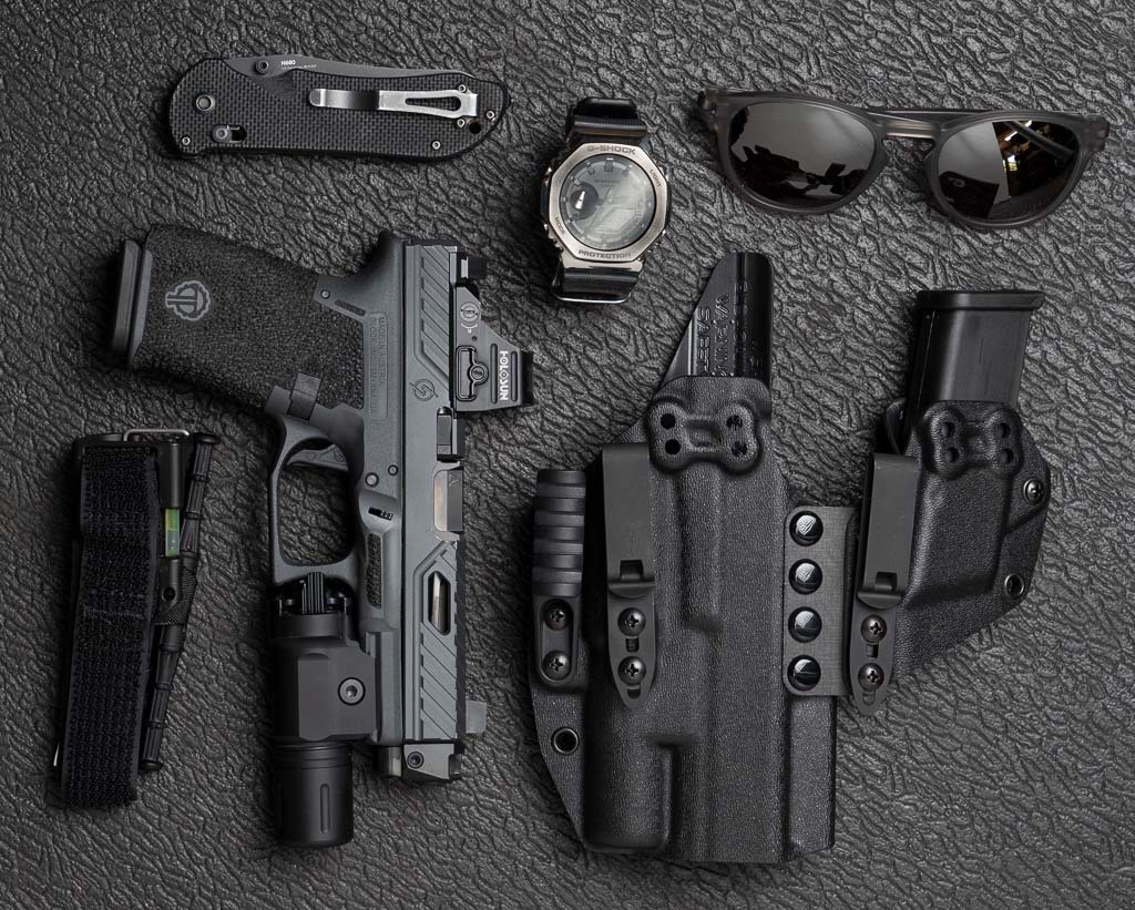 Everyday Carry load out including a Thyrm-branded arm, sunglasses, watch tourniquet, and holster.  Here, the CLENS protects a mounted light, but is otherwise invisible.