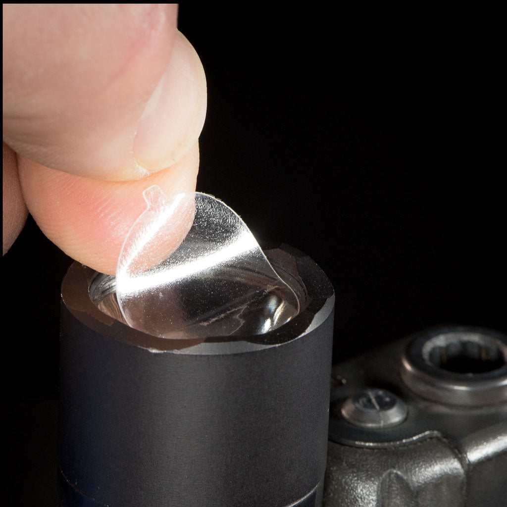 Index finger lifting a CLENS Lens Protector from a lens.