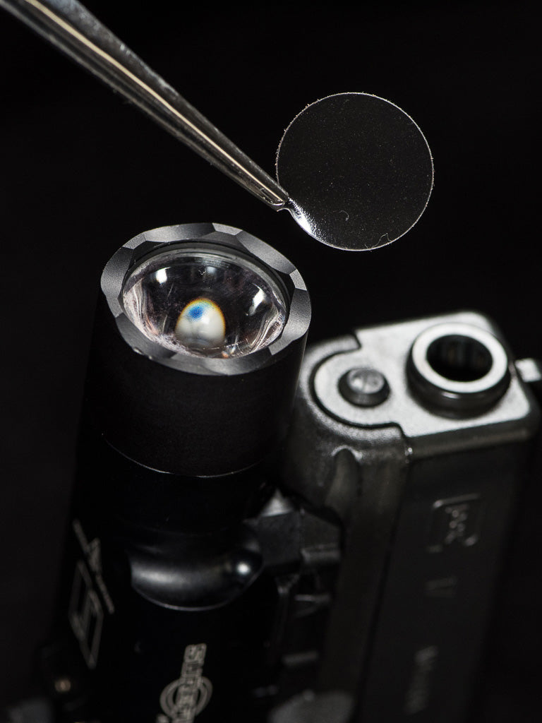 Tweezers positioning a CLENS Lens Protector above a lens.