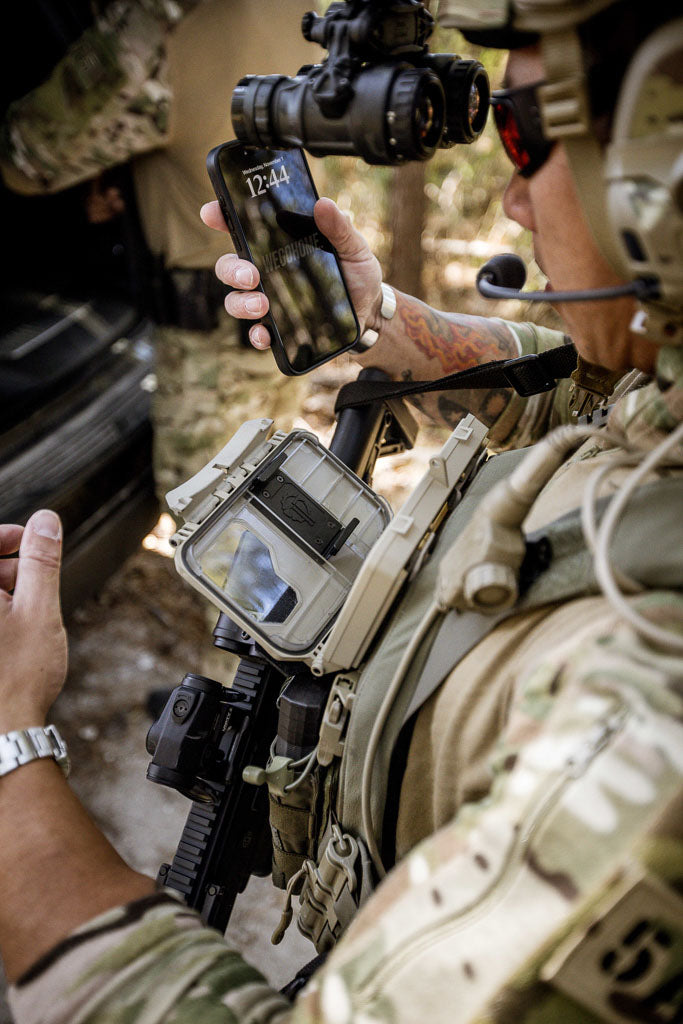 Person in military gear using an iPhone that he just removed from a DarkVault Comms 2.0 Critical Gear Case