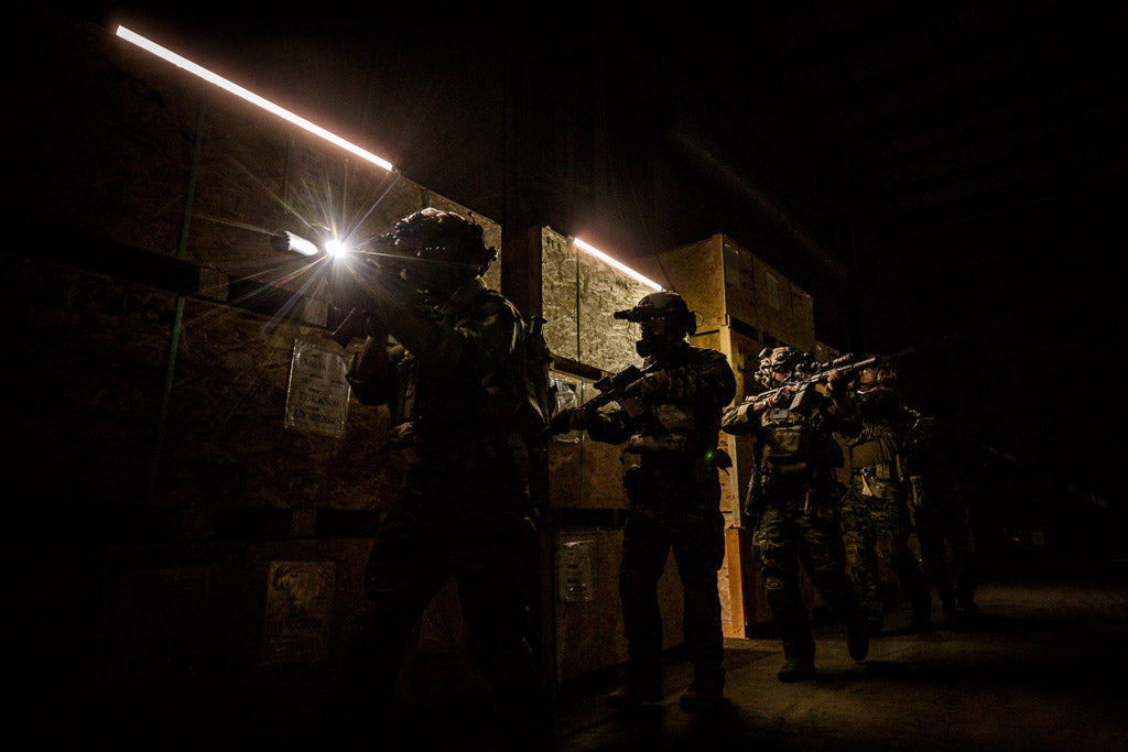 Silhouetted tactical team members with weapons and gear, operating in a dark warehouse with minimal lighting.