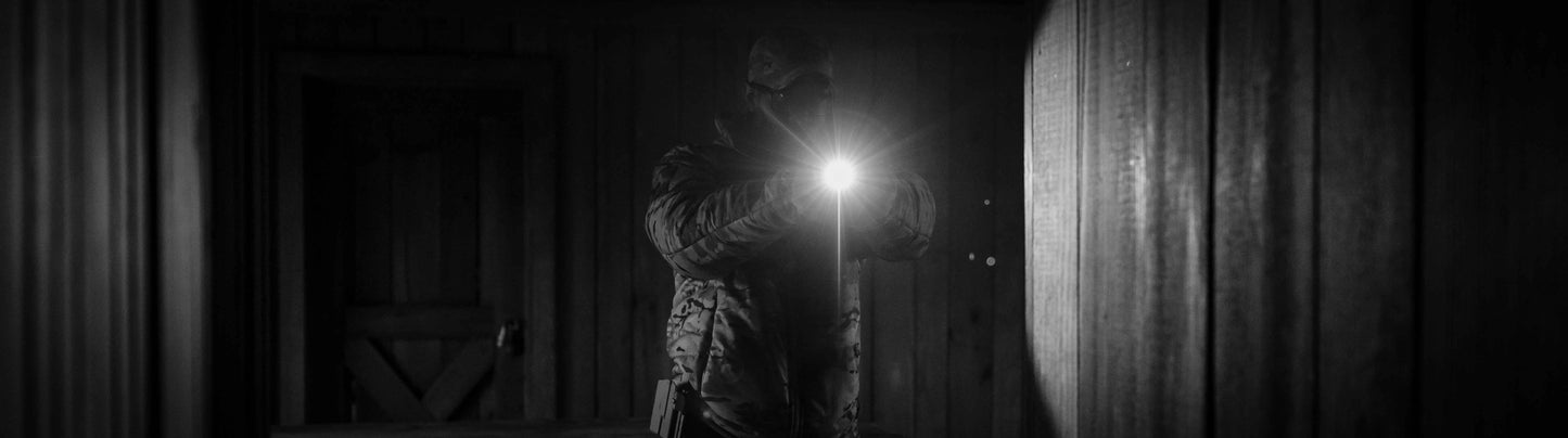 Person in camouflage holding a flashlight in a dark hallway