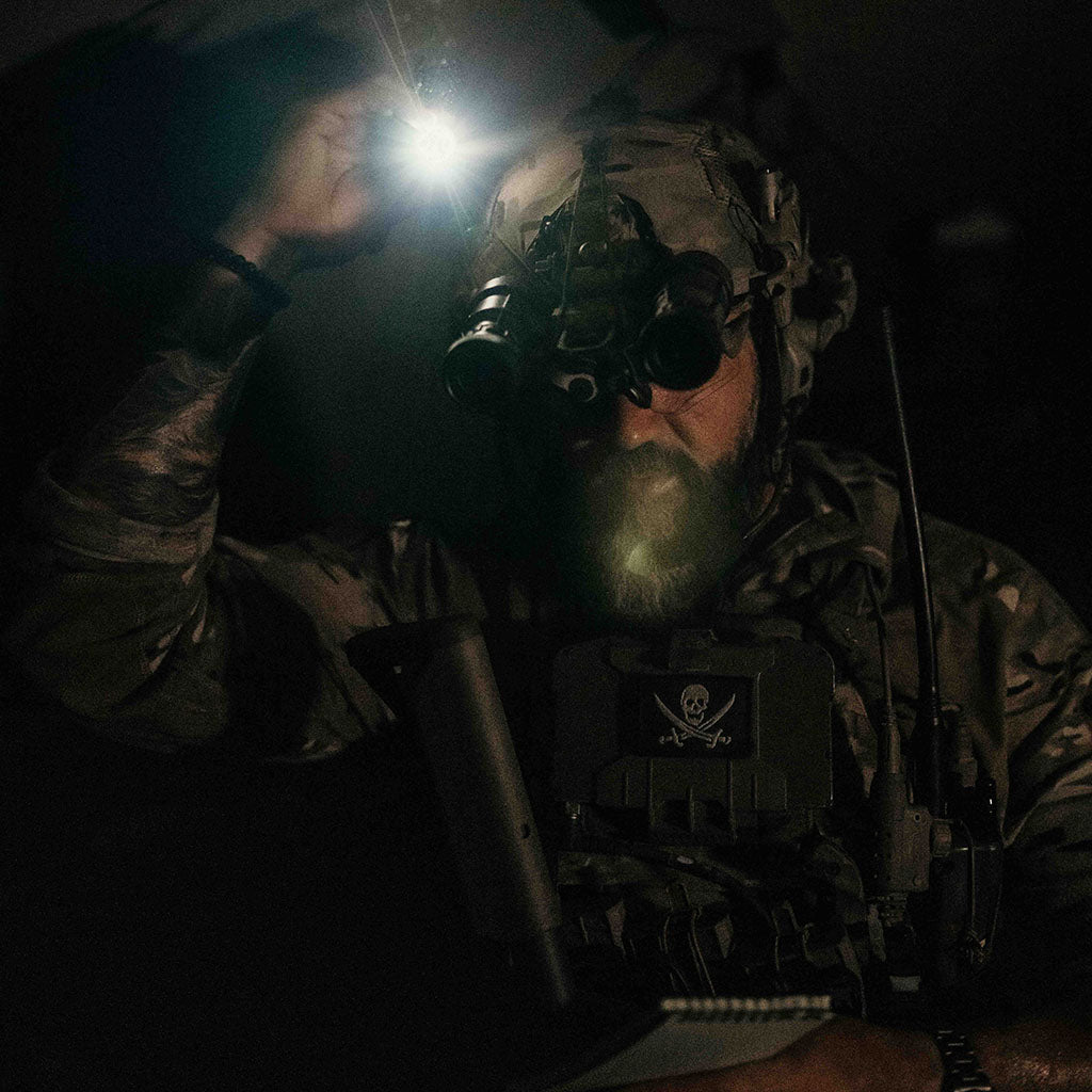 Person in tactical gear with a flashlight attached to their helmet with a Thyrm VariArc at night