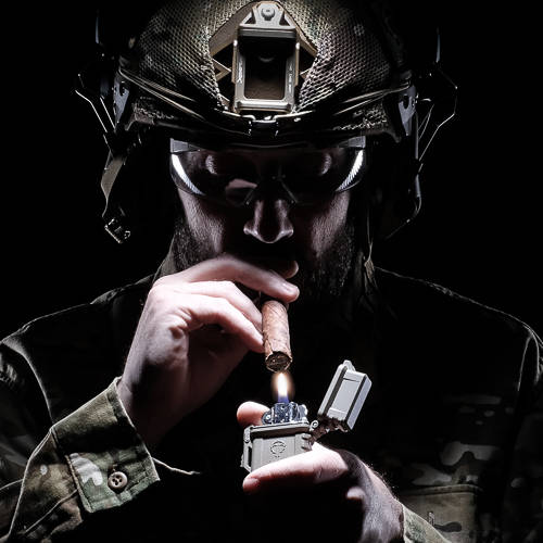 Person in tactical gear lighting a cigar with a PyroVault holding a classic Zippo fluid insert